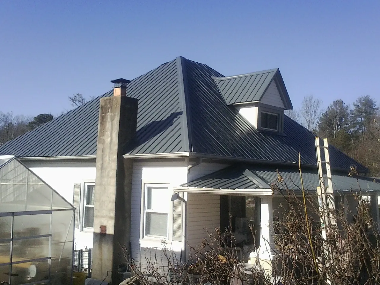 Dark blue standing seam metal roof on a white farmhouse with dormer — Slate & Tile Roof Repair by Roofing Brothers in Otsego