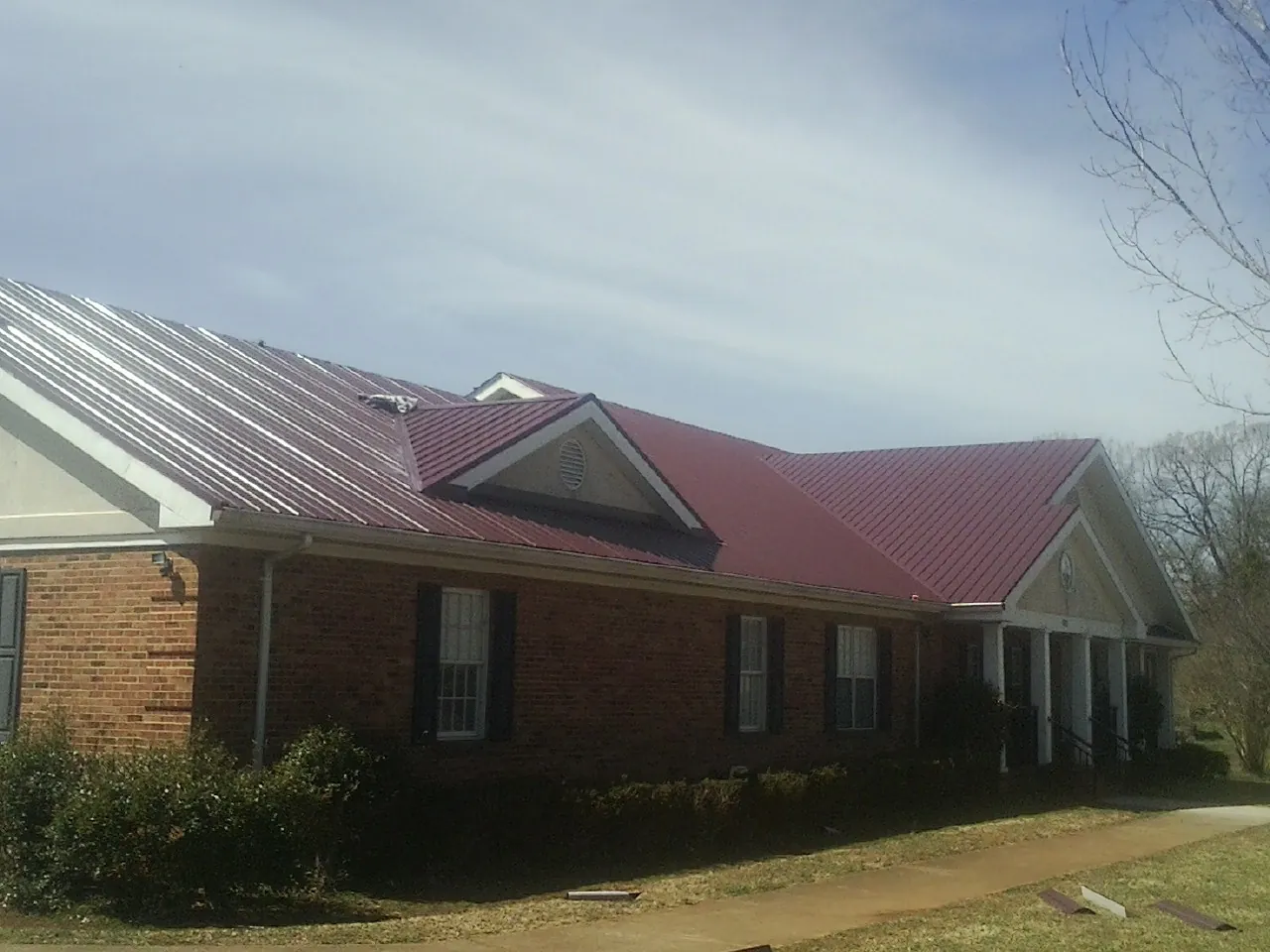 Red metal roof with gabled entries on a long brick building, from a Hail Damage Roof Repair job in Otsego