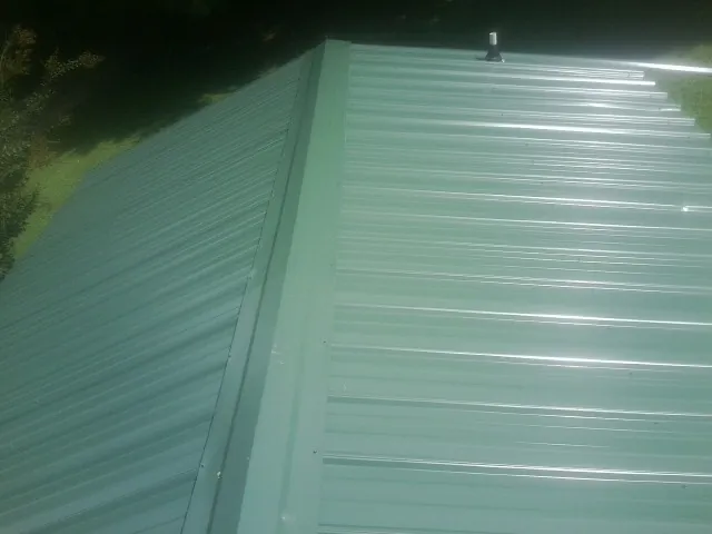 New green metal panels meeting at the ridge of a roof — Flat Roof Repair work by our crew in Otsego