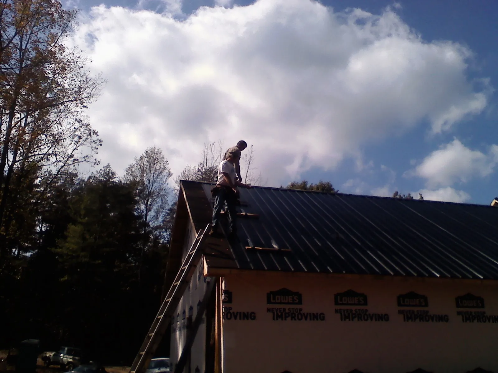 Roofer fastening dark metal panels high against a cloudy sky, from a Roof Inspection job in Otsego