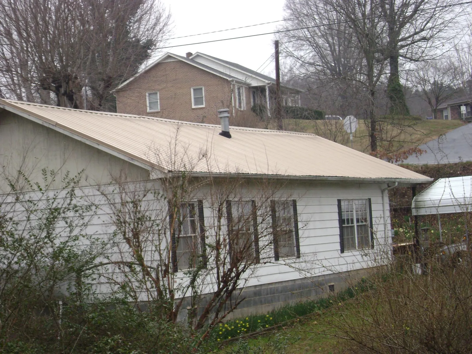 Tan metal roof on a white sided house set into a hillside — Commercial Roofing by Roofing Brothers in Otsego