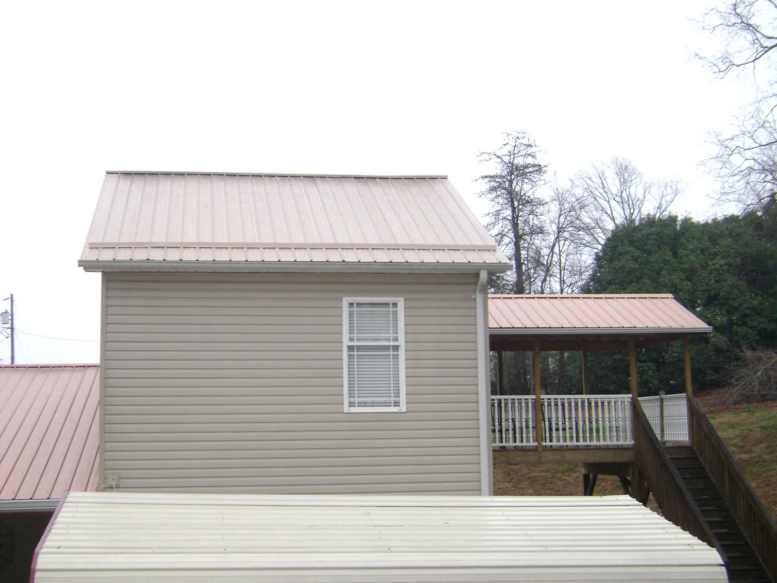 Tan metal roofs on a two story addition and attached porch, from a Roof Replacement job in Otsego