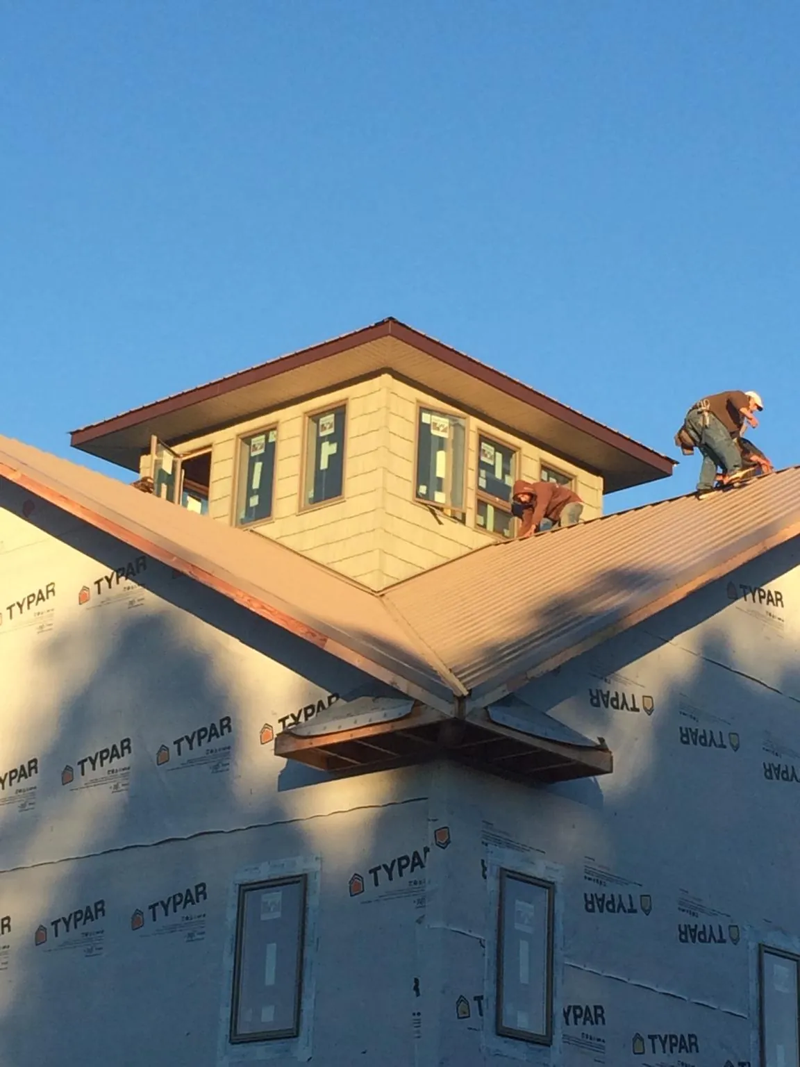 Roofers working around a rooftop cupola on a new metal roof at sunset — Roof Waterproofing in Otsego by Roofing Brothers